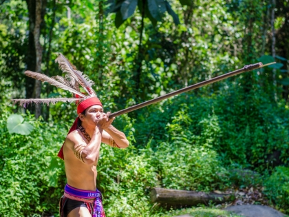 En mand klædt i traditionelt Murut-kostume holder en pusterør for munden i Mari Mari Cultural Village i Kota Kinabalu, Sabah